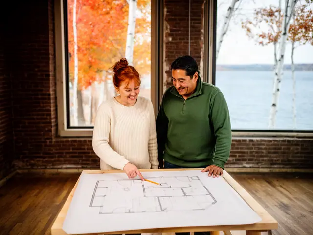 Two business partners smiling over a floor plan on a table in an empty brick room facing the lake